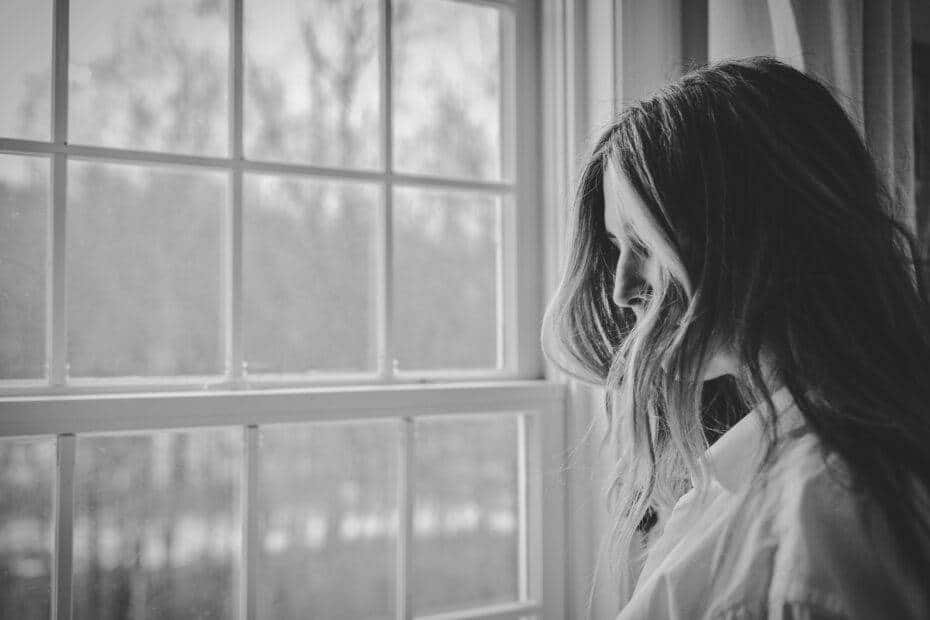 grayscale photo of woman near window